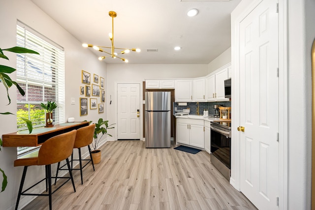 14742 Timbergreen Dr, Magnolia, TX 77355 - kitchen with stainless steel appliances, white cabinets, a chandelier, light wood finished floors, and light countertops