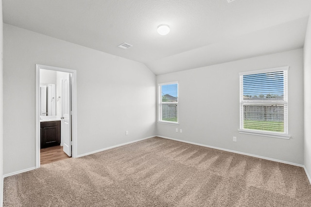 unfurnished bedroom featuring light carpet, baseboards, lofted ceiling, and connected bathroom
