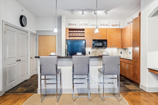 kitchen featuring fridge, black microwave, backsplash, a breakfast bar, and brown cabinets