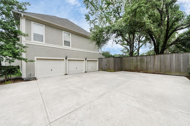 5701 Sugar Hill Dr, Houston, TX 77057 - view of side of home with an attached garage, stucco siding, driveway, fence, and roof with shingles