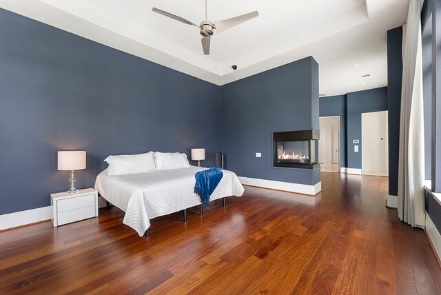3214 W Benders Landing Blvd, Spring, TX 77386 - bedroom with wood finished floors, a raised ceiling, baseboards, a multi sided fireplace, and a ceiling fan