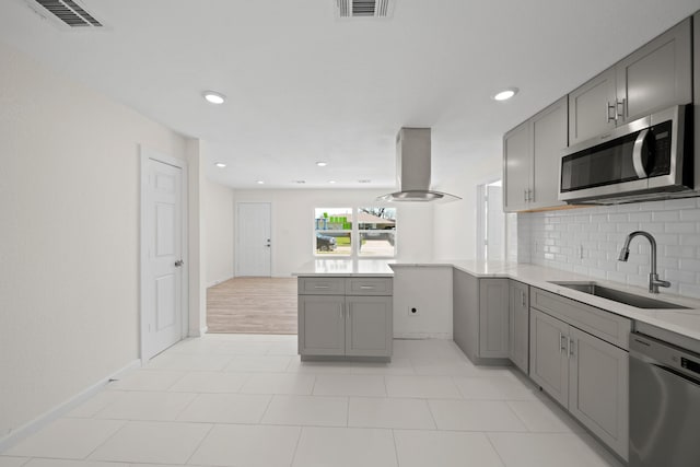 5763 Belneath St, Houston, TX 77033 - kitchen featuring stainless steel appliances, gray cabinets, island exhaust hood, a sink, and backsplash