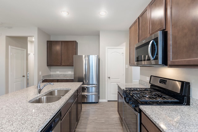24719 Colony Meadow Trl, Huffman, TX 77336 - kitchen with stainless steel appliances, a sink, light wood-style flooring, light stone counters, and dark brown cabinetry