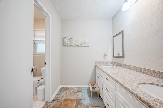 11607 Knobcrest Dr, Houston, TX 77070 - bathroom with double vanity, a textured ceiling, toilet, baseboards, and stone finish floors