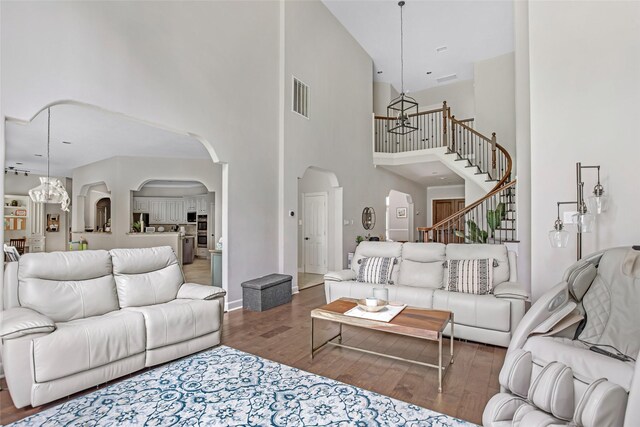living area featuring arched walkways, a high ceiling, wood finished floors, and stairway