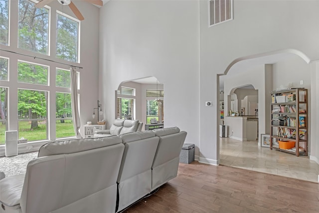 living area with arched walkways, ceiling fan, a towering ceiling, wood finished floors, and baseboards