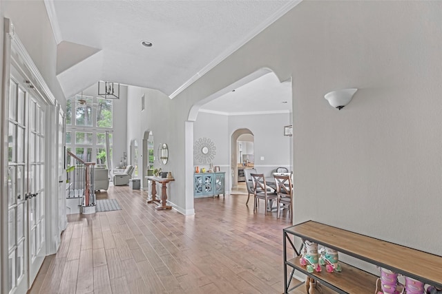 entrance foyer with arched walkways, crown molding, wood finished floors, french doors, and a chandelier