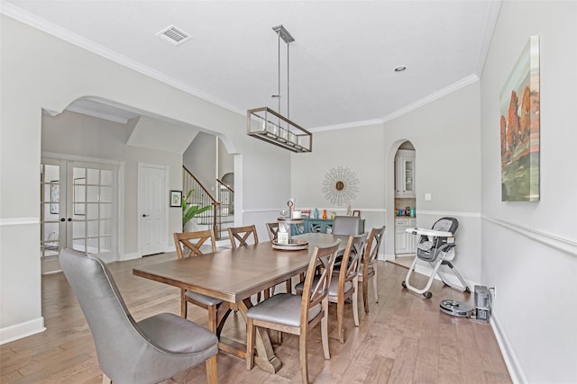 dining area with arched walkways, light wood-style flooring, ornamental molding, stairs, and baseboards