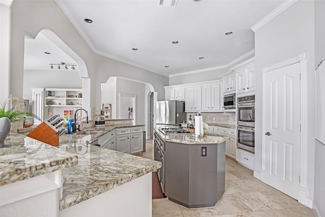 kitchen featuring a sink, stainless steel appliances, tasteful backsplash, a kitchen island, and ornamental molding