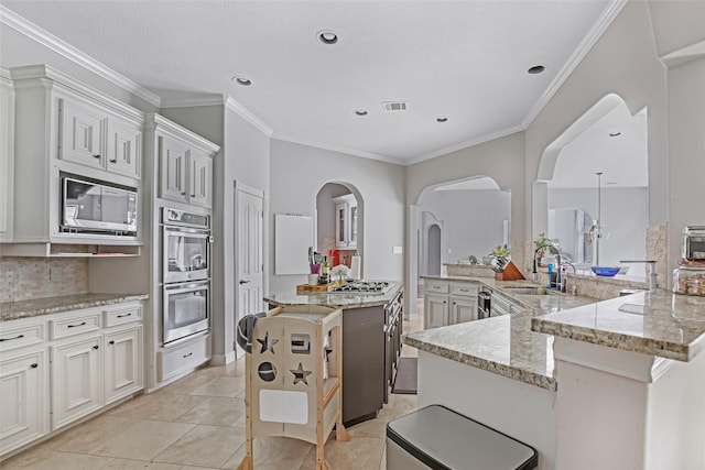 kitchen with stainless steel appliances, a sink, arched walkways, a spacious island, and light stone countertops