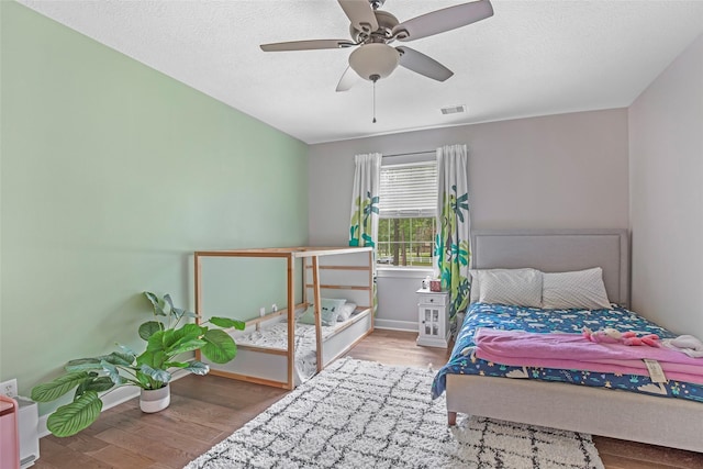 bedroom with wood finished floors, baseboards, ceiling fan, and a textured ceiling