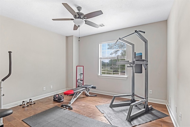 workout area with wood finished floors, a ceiling fan, a textured ceiling, and baseboards