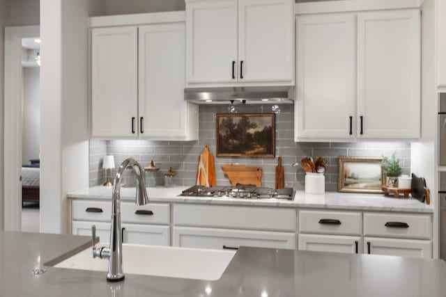 19720 Holly Creek Bnd, Magnolia, TX 77355 - kitchen with white cabinetry, backsplash, stainless steel gas cooktop, and under cabinet range hood