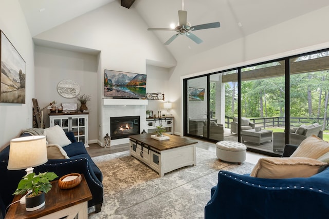 19720 Holly Creek Bnd, Magnolia, TX 77355 - living room featuring high vaulted ceiling, a ceiling fan, beamed ceiling, a tile fireplace, and light wood-style flooring