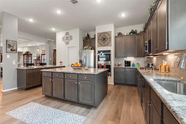 3314 Bastian Rd, Dickinson, TX 77539 - kitchen with stainless steel appliances, a sink, light wood-type flooring, dark brown cabinetry, and a kitchen island