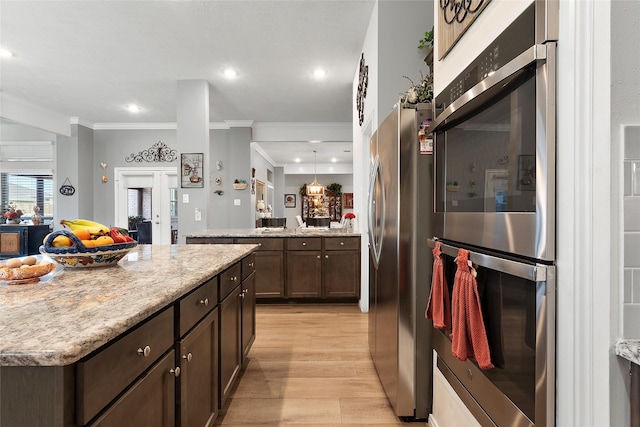 3314 Bastian Rd, Dickinson, TX 77539 - kitchen with stainless steel appliances, light wood finished floors, dark brown cabinets, ornamental molding, and a peninsula
