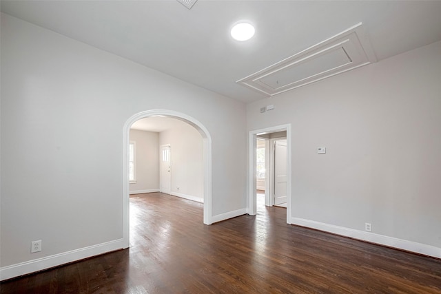 spare room featuring attic access, dark wood-style floors, baseboards, and arched walkways