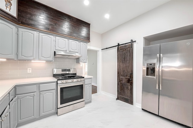 kitchen with stainless steel appliances, under cabinet range hood, a barn door, light countertops, and tasteful backsplash