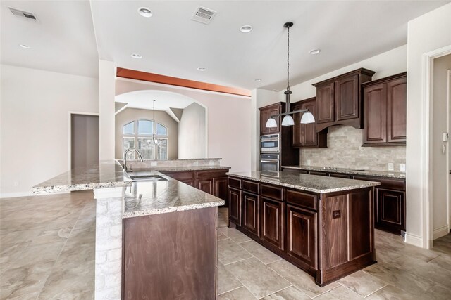 23335 Robinson Pond Dr, New Caney, TX 77357 - kitchen featuring a large island, a sink, decorative backsplash, arched walkways, and hanging light fixtures