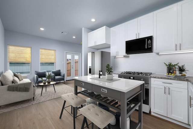 18832 Elegance Ave, Spring, TX 77379 - kitchen featuring appliances with stainless steel finishes, open floor plan, wood finished floors, decorative backsplash, and white cabinets