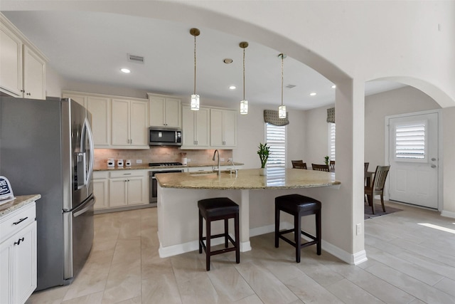 kitchen with stainless steel appliances, a breakfast bar area, a sink, tasteful backsplash, and light stone countertops