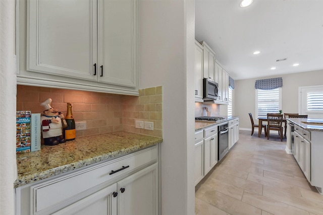 kitchen with appliances with stainless steel finishes, backsplash, white cabinets, recessed lighting, and light stone counters