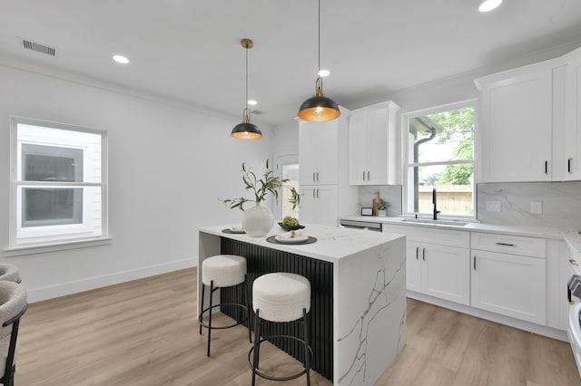kitchen with a sink, a kitchen island, a breakfast bar area, light wood-type flooring, and ornamental molding