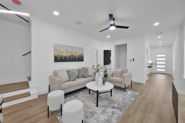 living room with a ceiling fan, light wood-type flooring, stairs, baseboards, and ornamental molding