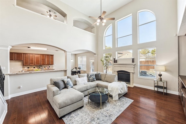 11405 Starlight Bay St, Pearland, TX 77584 - living room featuring arched walkways, a ceiling fan, ornate columns, a towering ceiling, and dark wood finished floors