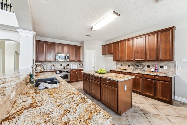 11405 Starlight Bay St, Pearland, TX 77584 - kitchen featuring a sink, stainless steel appliances, tasteful backsplash, light stone counters, and arched walkways