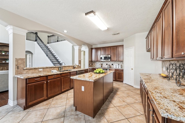 11405 Starlight Bay St, Pearland, TX 77584 - kitchen featuring appliances with stainless steel finishes, a sink, decorative columns, backsplash, and a center island