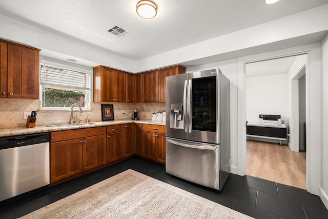 13919 Kimberley Ln, Houston, TX 77079 - kitchen featuring stainless steel appliances, a sink, decorative backsplash, dark tile patterned floors, and brown cabinets