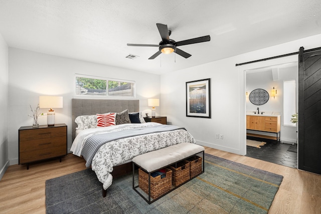 13919 Kimberley Ln, Houston, TX 77079 - bedroom featuring wood finished floors, a barn door, a sink, and baseboards