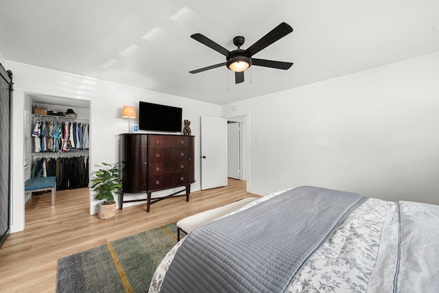 13919 Kimberley Ln, Houston, TX 77079 - bedroom featuring light wood-type flooring, a spacious closet, a barn door, ceiling fan, and a closet