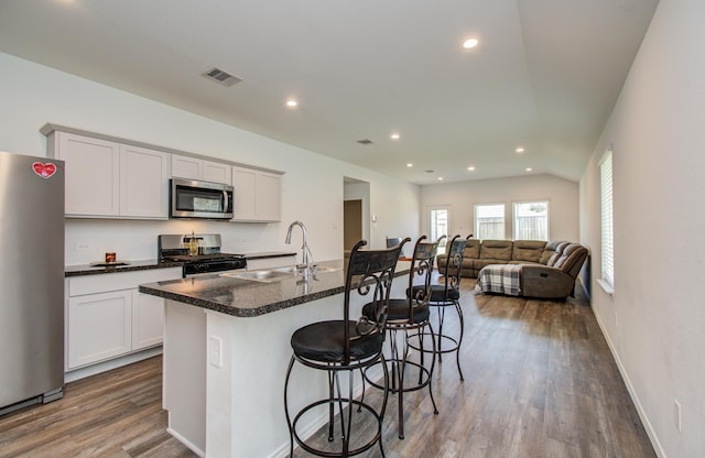 kitchen with appliances with stainless steel finishes, a sink, wood finished floors, a breakfast bar area, and recessed lighting
