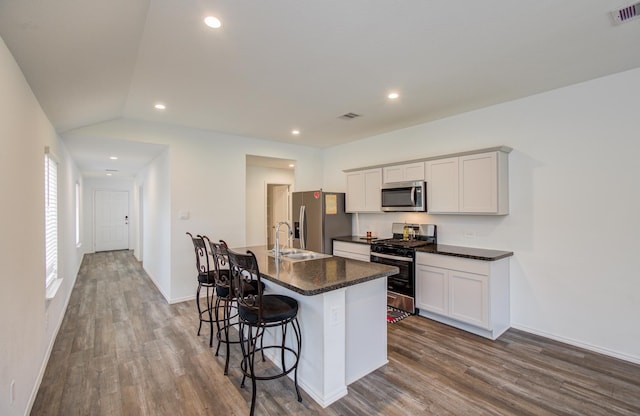 kitchen featuring appliances with stainless steel finishes, dark wood-type flooring, dark countertops, a breakfast bar area, and recessed lighting