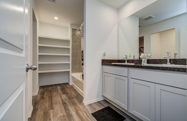 full bathroom with wood finished floors, double vanity, a walk in closet,  shower combination, and recessed lighting