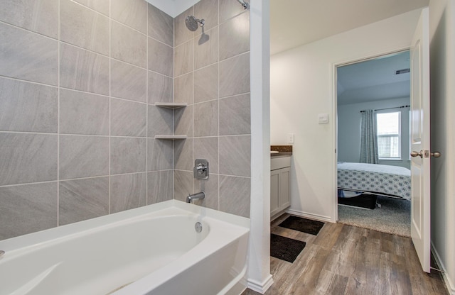 ensuite bathroom featuring wood finished floors, vanity, bathtub / shower combination, and baseboards
