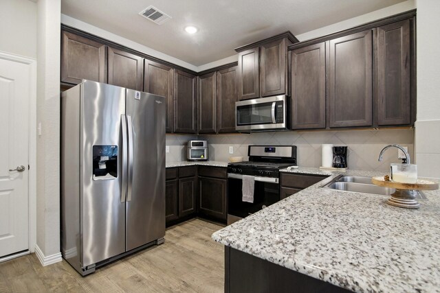 15863 Sundew Prairie Dr, Humble, TX 77346 - kitchen featuring appliances with stainless steel finishes, dark brown cabinets, light wood-type flooring, backsplash, and a sink