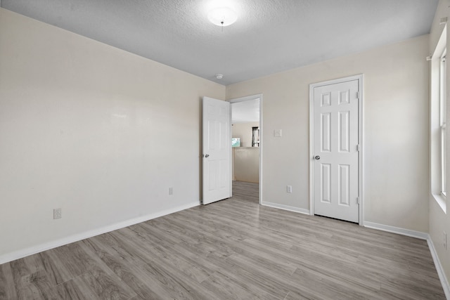 8006 Saffron Ln, Baytown, TX 77521 - unfurnished bedroom featuring light wood-type flooring, baseboards, and a textured ceiling