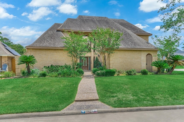 view of front of home featuring brick siding, a front yard, and roof with shingles