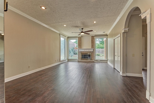 unfurnished living room with ceiling fan, a fireplace, arched walkways, dark wood-style flooring, and crown molding