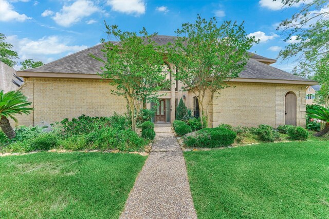 view of front of property with brick siding, a front yard, and roof with shingles