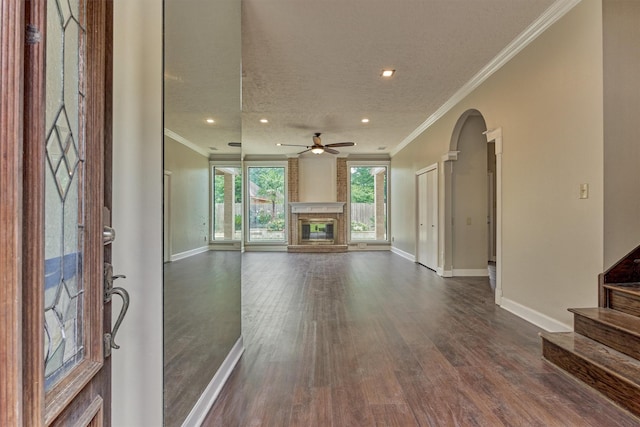 unfurnished living room with baseboards, crown molding, a fireplace, arched walkways, and recessed lighting