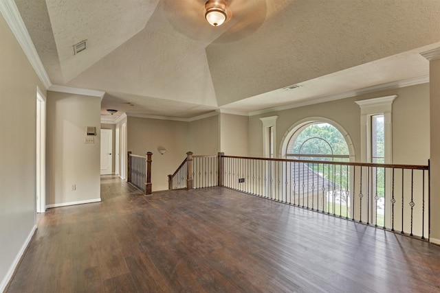 empty room featuring wood finished floors, a textured ceiling, ornamental molding, and baseboards