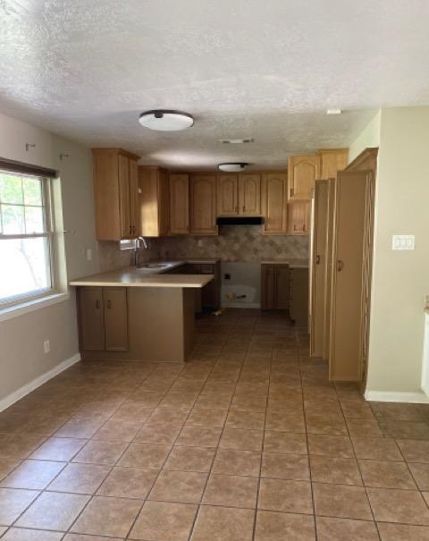404 Friery St, Dayton, TX 77535 - kitchen with a peninsula, a textured ceiling, light tile patterned floors, under cabinet range hood, and a sink