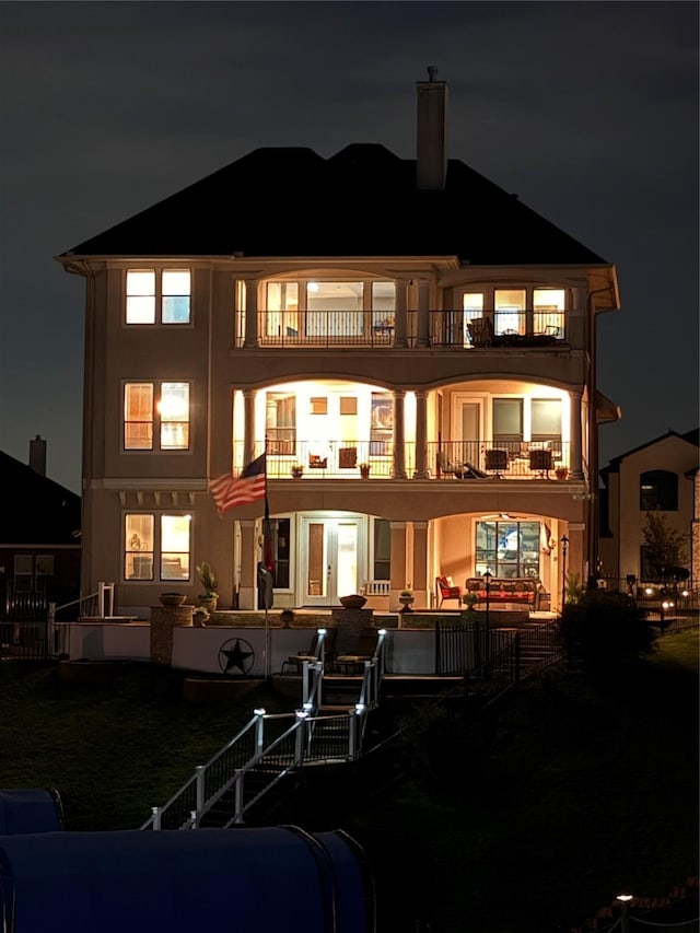 12590 St Ann Ct, Willis, TX 77318 - back of house at twilight featuring a balcony, a chimney, and stucco siding