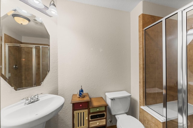 full bathroom featuring a sink, a stall shower, toilet, and a textured wall
