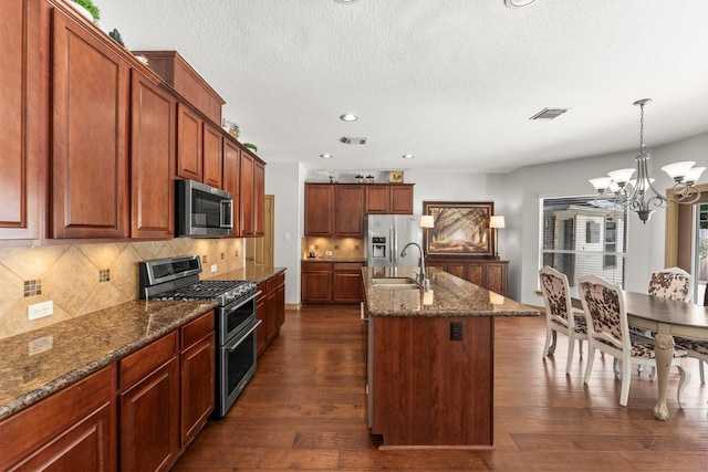 kitchen featuring appliances with stainless steel finishes, a sink, dark wood-type flooring, a chandelier, and a kitchen island with sink