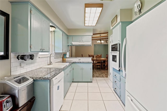 kitchen with white appliances, a sink, light tile patterned floors, under cabinet range hood, and backsplash
